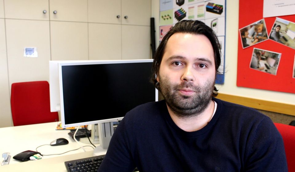 Ein Mann sitzt an einem Schreibtisch und blickt in die Kamera