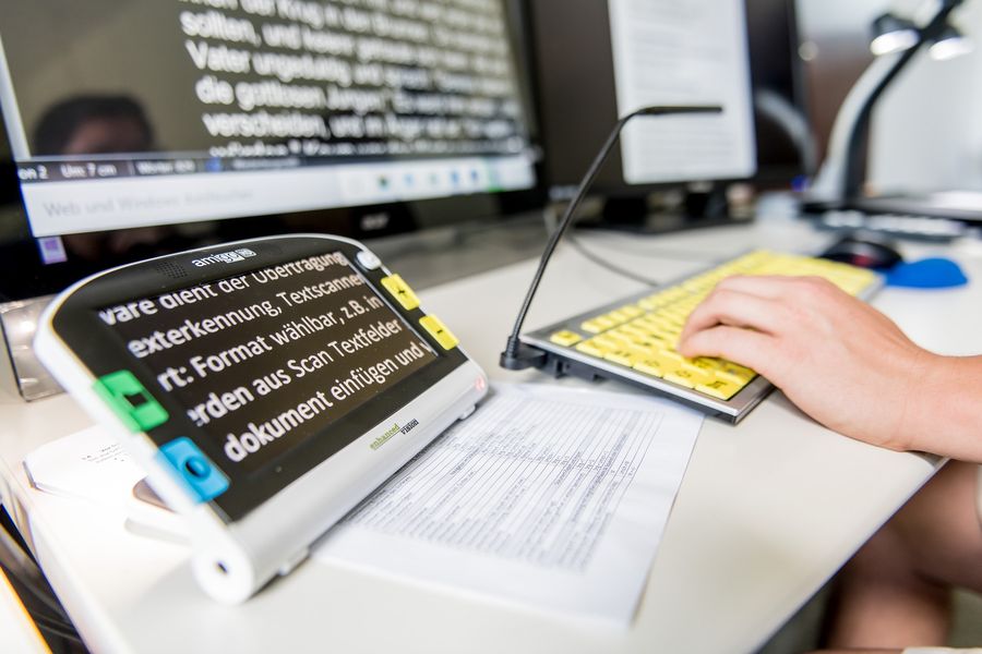 Eine Person arbeitet am Computer und nutze elektronische Hilfsmittel für Blinde und Sehbehinderte